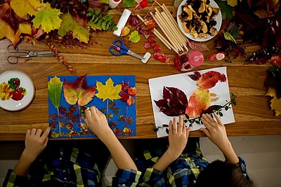 Zwei Kindern basteln herbstliche Bilder mit Blättern und Eicheln