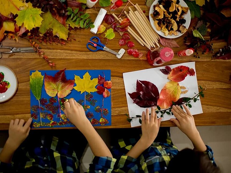 Zwei Kindern basteln herbstliche Bilder mit Blättern und Eicheln