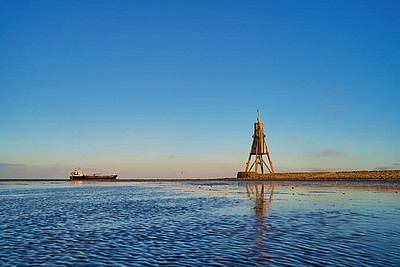 Sonnenaufgang an der Kugelbake in Cuxhaven mit einem Schiff im Hintergrund