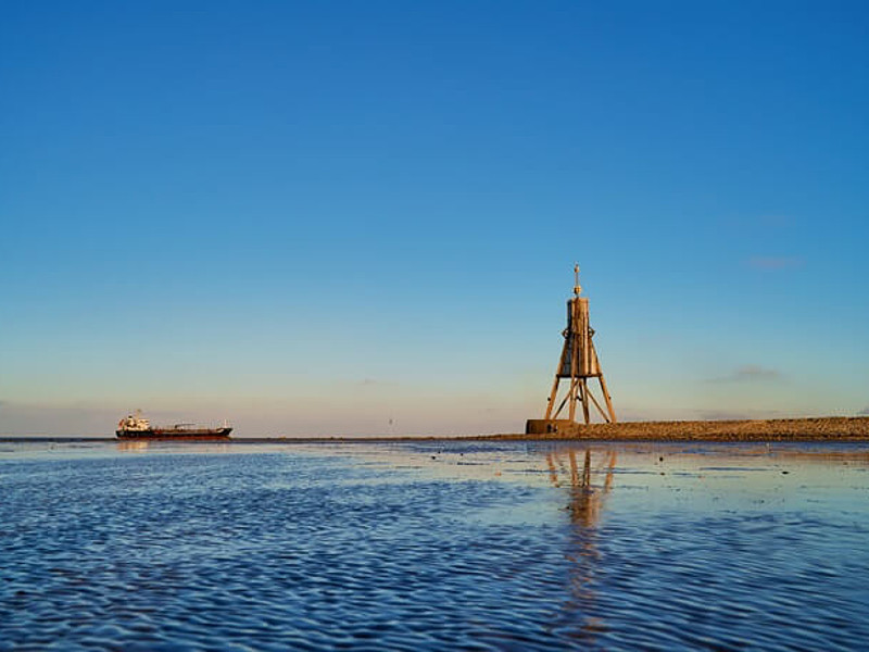 Sonnenaufgang an der Kugelbake in Cuxhaven mit einem Schiff im Hintergrund