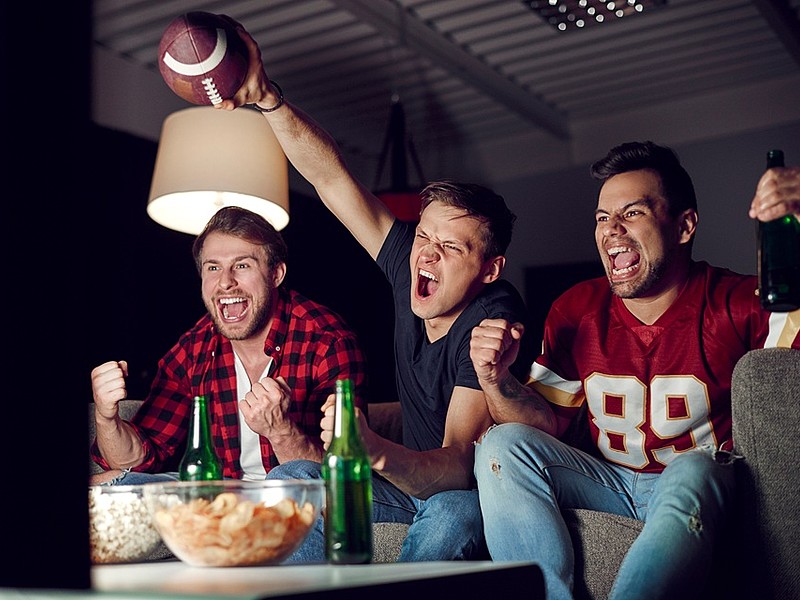 3 Männer schaurn auf dem Sofa ein Footballspiel mit passenen Snacks und Getränken